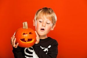 Boy on orange background, looking at his jack o'lantern.